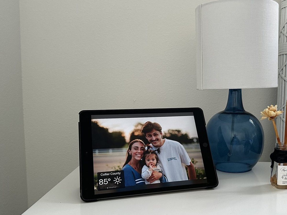 An iPad photo frame on a bedside table next to a lamp
