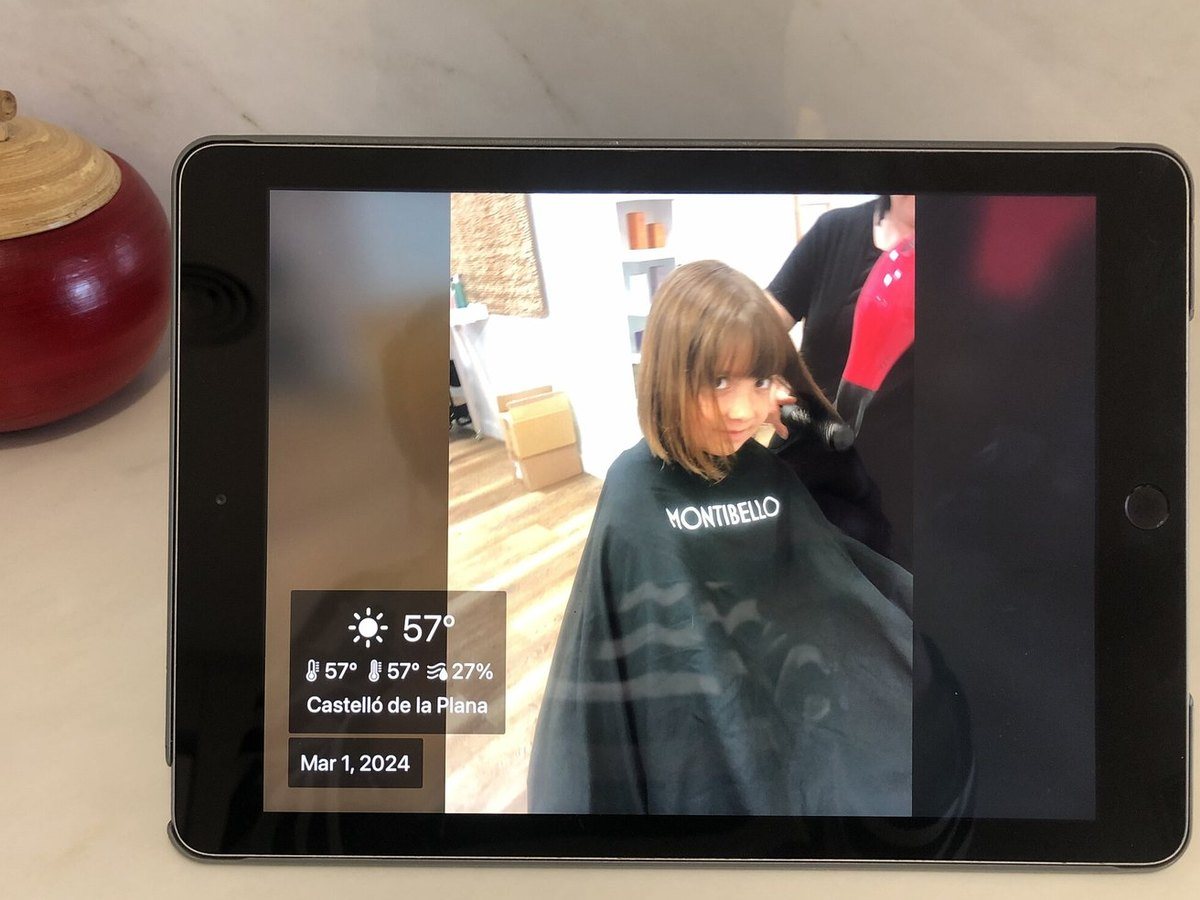 An iPad photo frame on a kitchen counter showing a child at the hairdresser