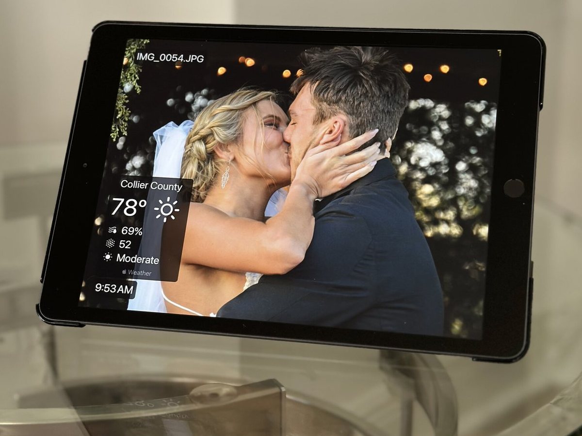 An iPad photo frame on a glass table showing a wedding photo